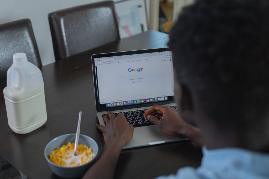 pexels-photo-7350921 A person browsing Google on a laptop while having cereal breakfast at the table.